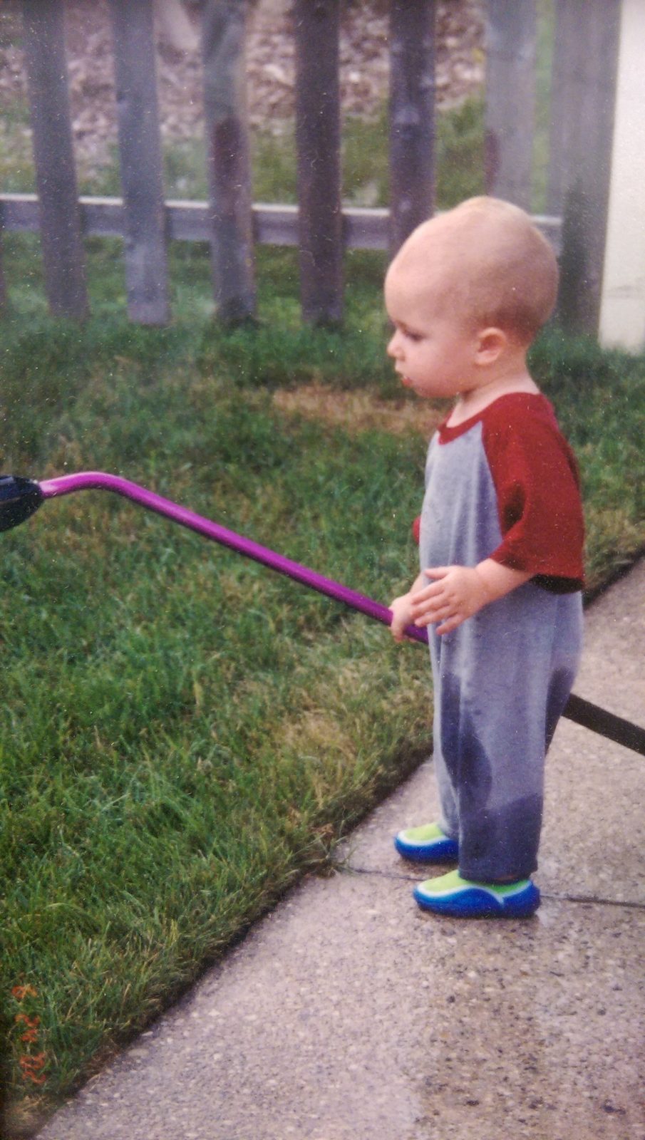 Justin as a toddler holding a garden hose on the sidewalk