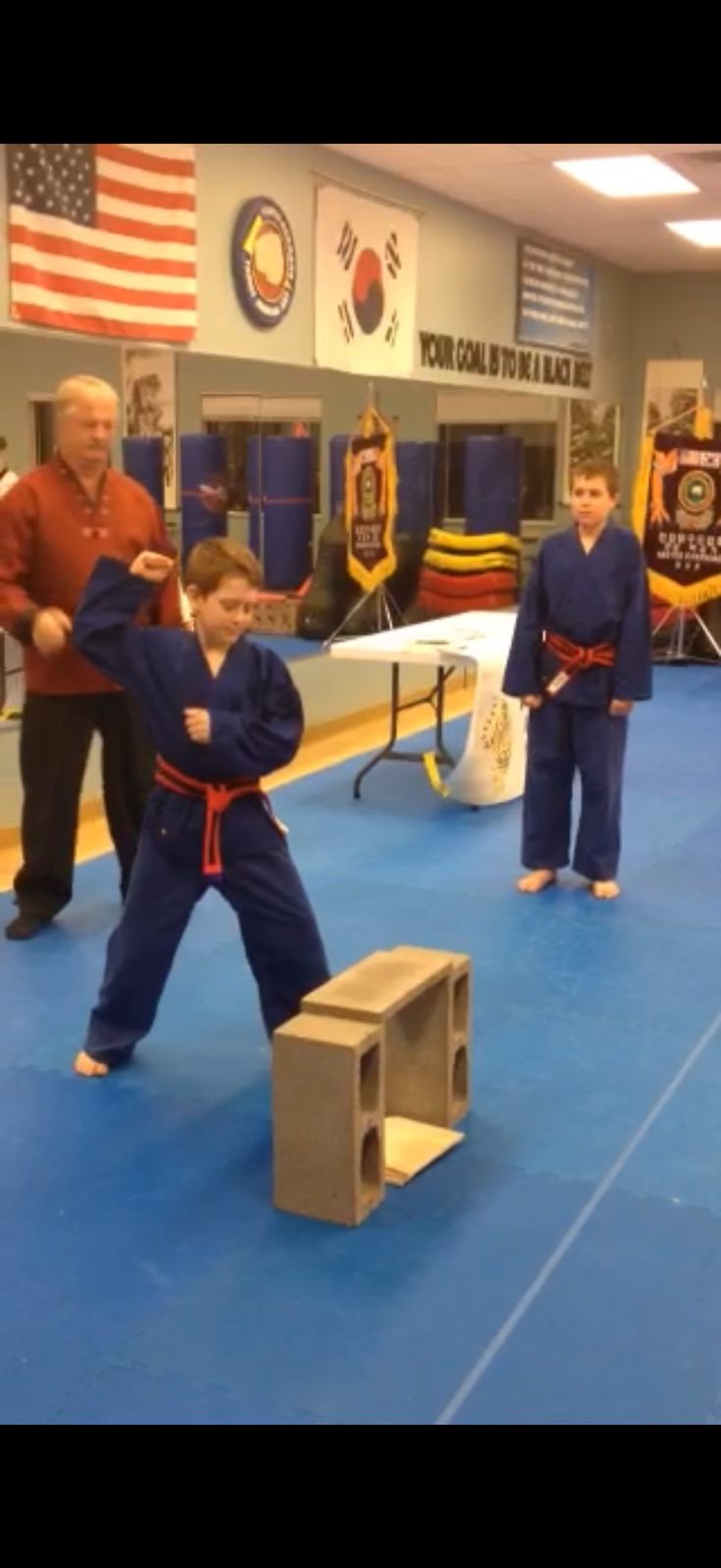 Justin in a karate gi breaking a board, black-belt banner behind him
